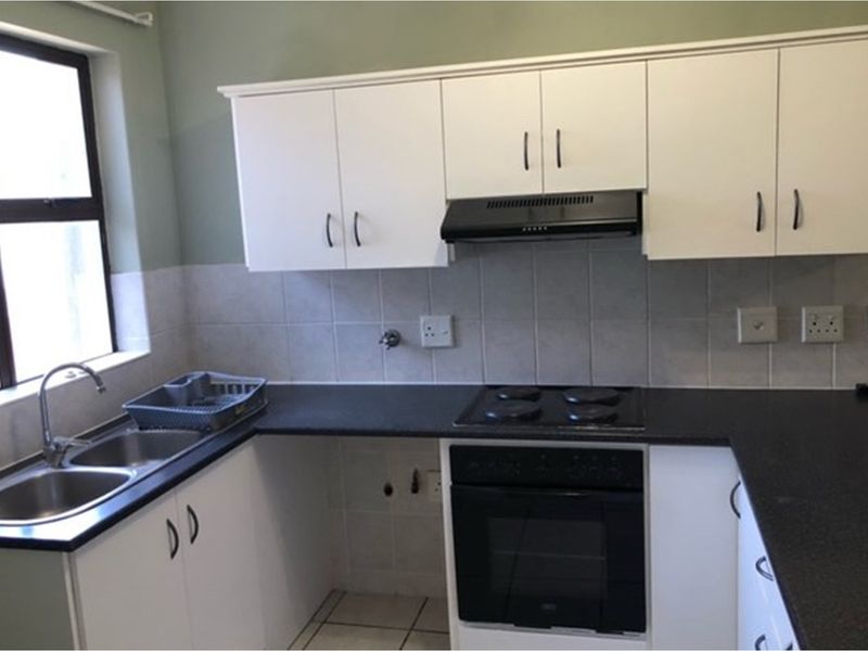 Functional kitchen featuring white cabinetry, dark countertops, a built-in oven with hob, extractor fan, and a double stainless steel sink.