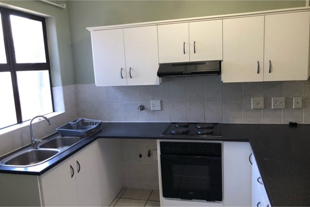 Functional kitchen featuring white cabinetry, dark countertops, a built-in oven with hob, extractor fan, and a double stainless steel sink.