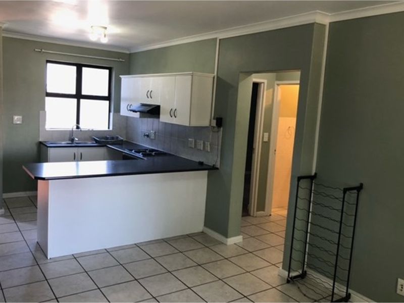 Open-plan kitchen featuring a breakfast bar, built-in cabinetry, integrated hob, and extractor fan, with tiled flooring throughout the living area.