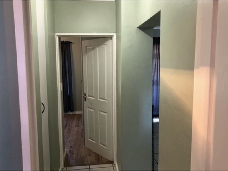 A view through a hallway connecting to adjacent rooms, featuring tiled flooring and painted interior walls.