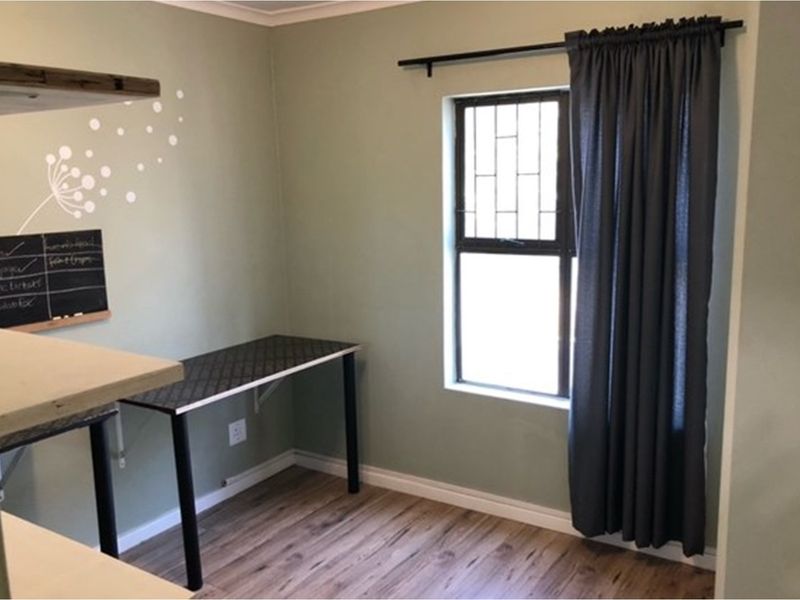 A functional office space featuring wood-look flooring, a built-in desk area, and a window with security bars.