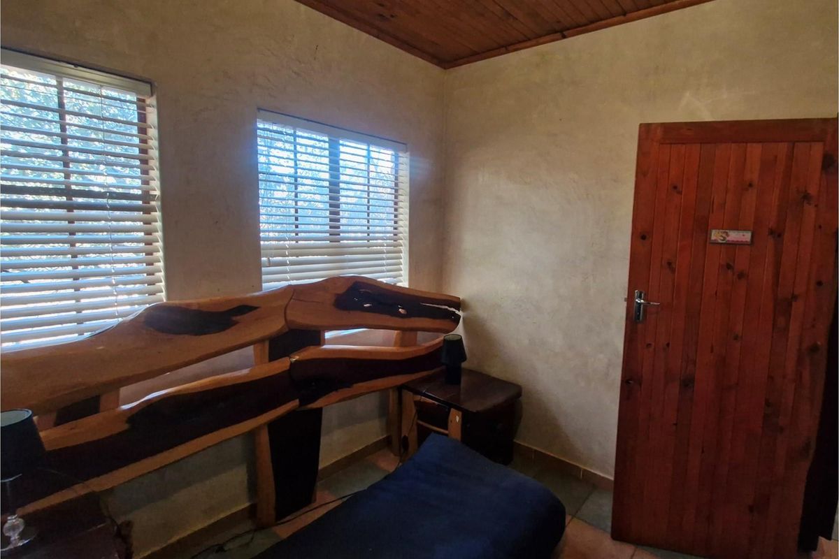A bedroom featuring rustic timber ceiling paneling, wooden door, and dual windows with fitted blinds.
