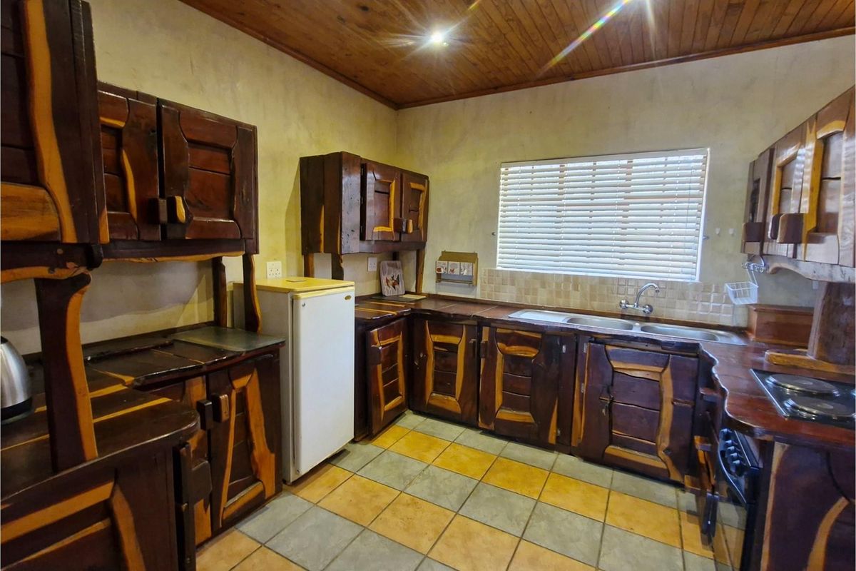 A rustic kitchen featuring custom dark wood cabinetry, tiled countertops, a double basin sink, and a timber-clad ceiling.