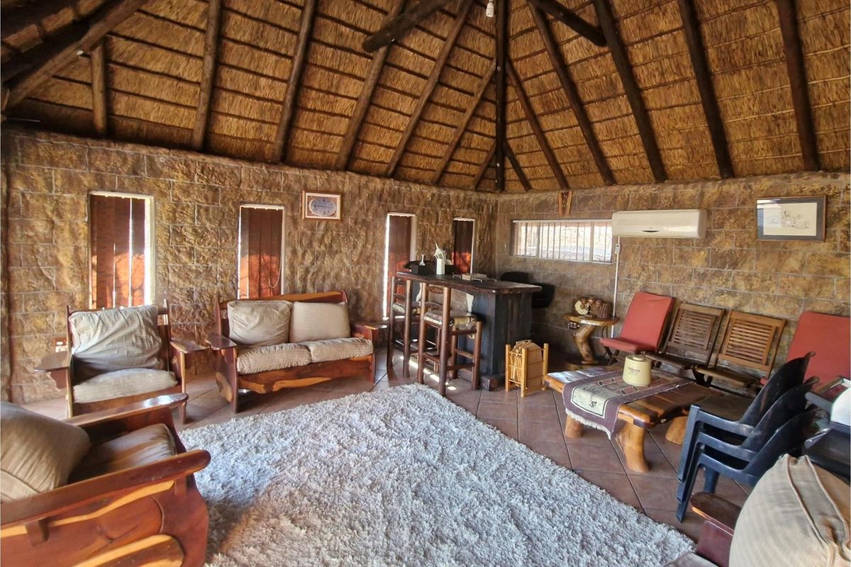 Spacious living area featuring a high vaulted thatched roof, exposed timber beams, and rustic stone-clad walls with integrated air conditioning.