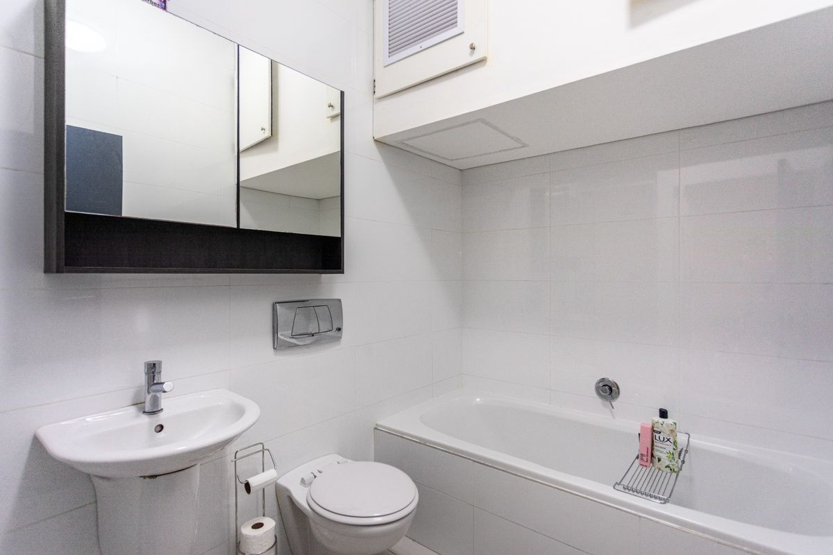 A compact bathroom featuring white wall tiles, a pedestal basin, a wall-mounted toilet with a concealed cistern, and a built-in bathtub.