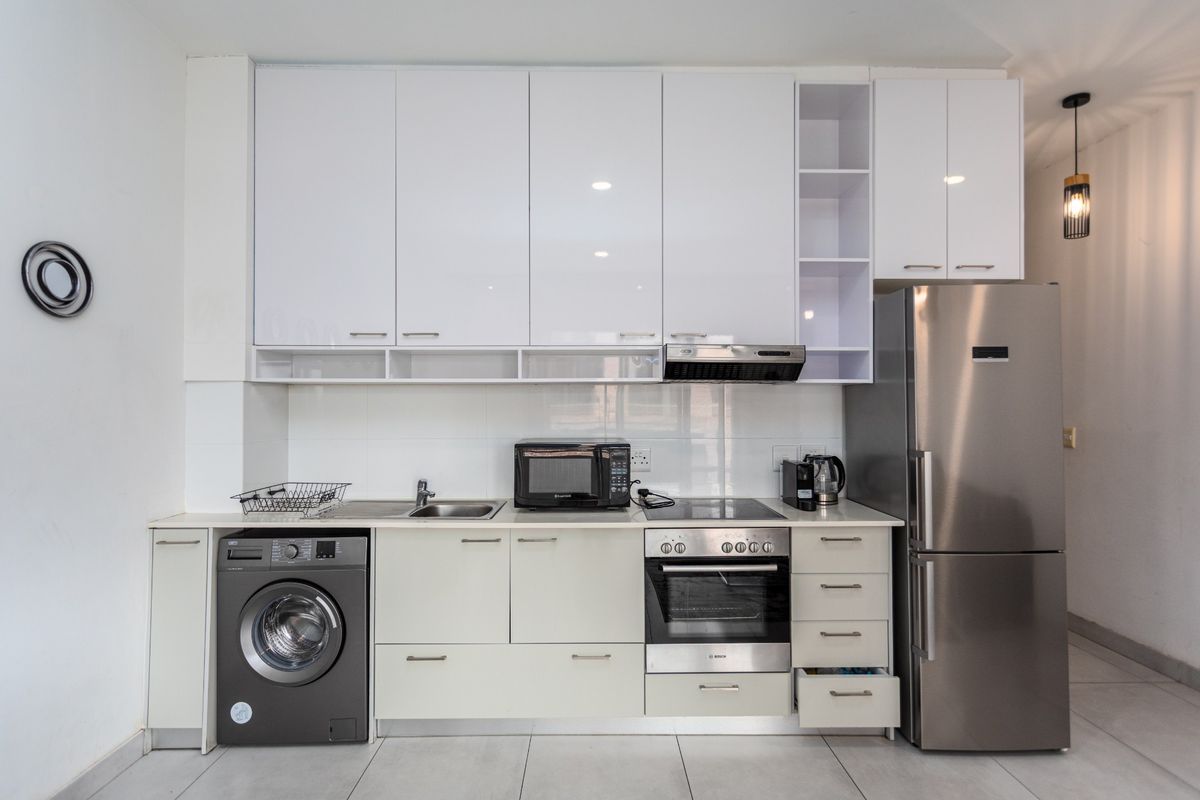 Modern kitchen featuring white high-gloss cabinetry, integrated stainless steel oven, electric hob, extractor fan, and space for a washing machine and refrigerator.