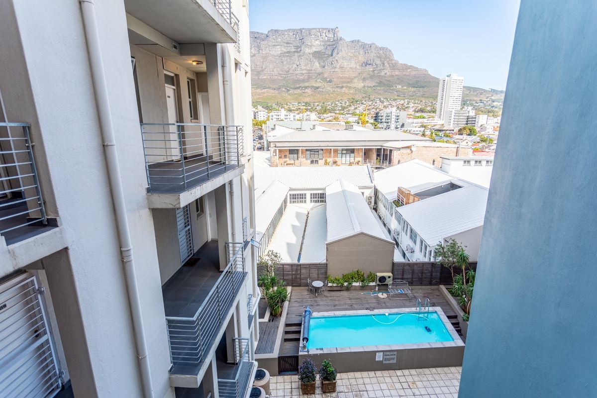 Elevated view of the apartment complex courtyard featuring a swimming pool, wooden decking, and surrounding balconies with mountain views in the background.