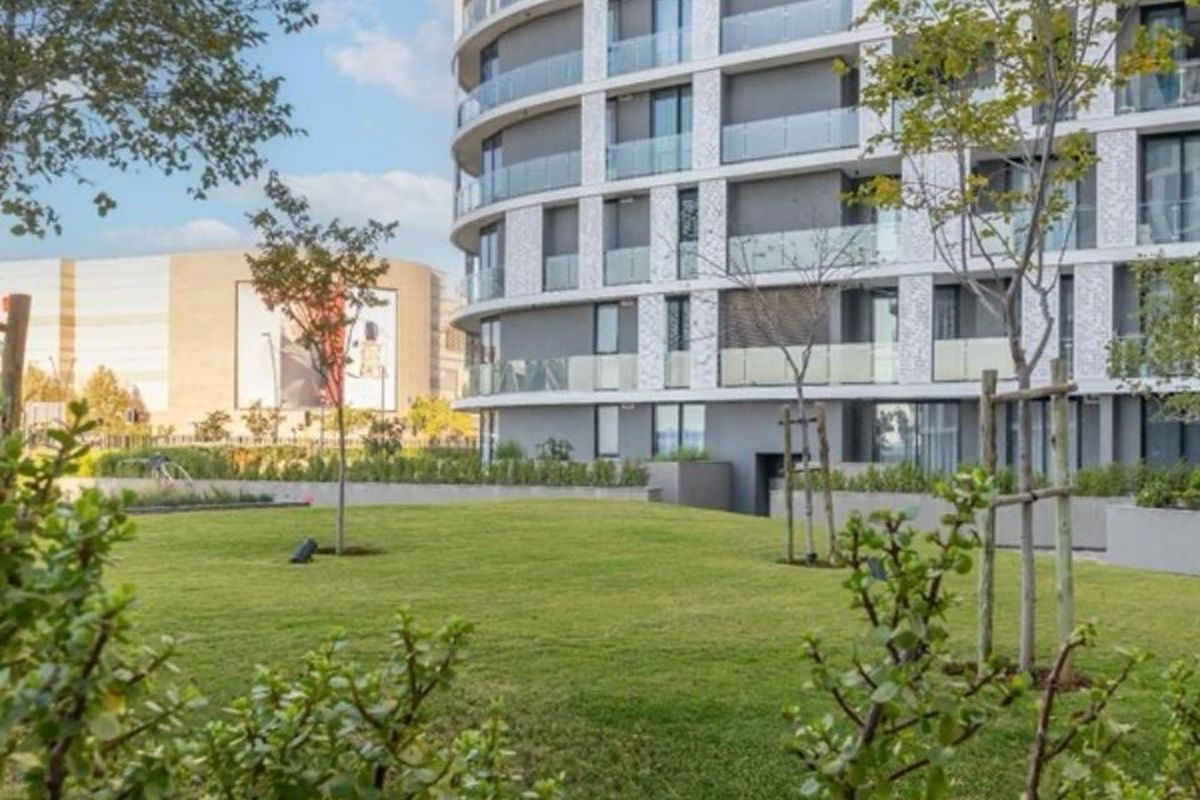 A view of the modern apartment building exterior featuring glass balconies and well-maintained landscaped garden areas.