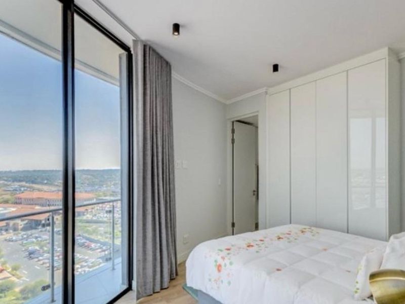 Modern bedroom featuring floor-to-ceiling glass doors with balcony access, built-in wardrobes, and contemporary recessed lighting.