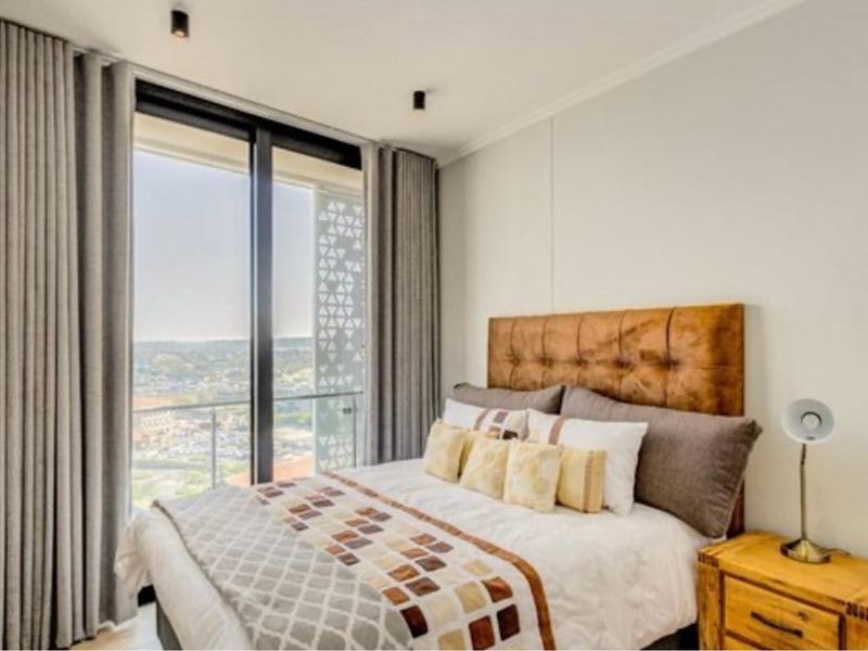 Modern bedroom featuring floor-to-ceiling windows with balcony access, providing ample natural light and expansive views.