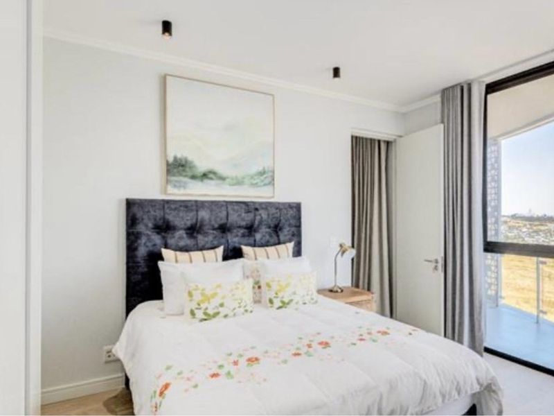 A bright, modern bedroom featuring laminate flooring, recessed ceiling lighting, and a large sliding glass door providing access to a private balcony.