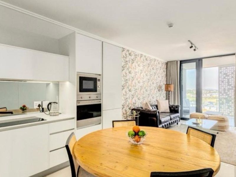 Modern open-plan living area featuring a sleek kitchen with integrated appliances, floral feature wall, and direct access to a private balcony.