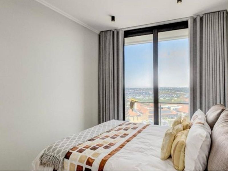 A modern bedroom featuring floor-to-ceiling windows with sliding glass doors, offering expansive views and ample natural light.