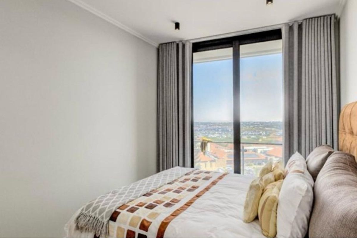 A modern bedroom featuring floor-to-ceiling windows with sliding glass doors, offering expansive views and ample natural light.