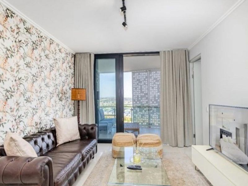 A well-lit living room featuring tiled flooring, decorative wallpaper, and large sliding glass doors providing direct access to an outdoor balcony.