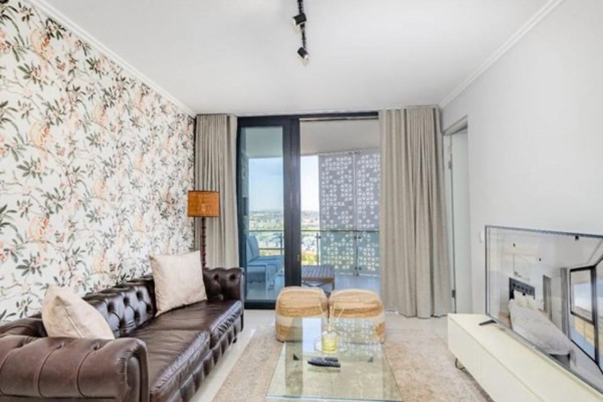 A well-lit living room featuring tiled flooring, decorative wallpaper, and large sliding glass doors providing direct access to an outdoor balcony.