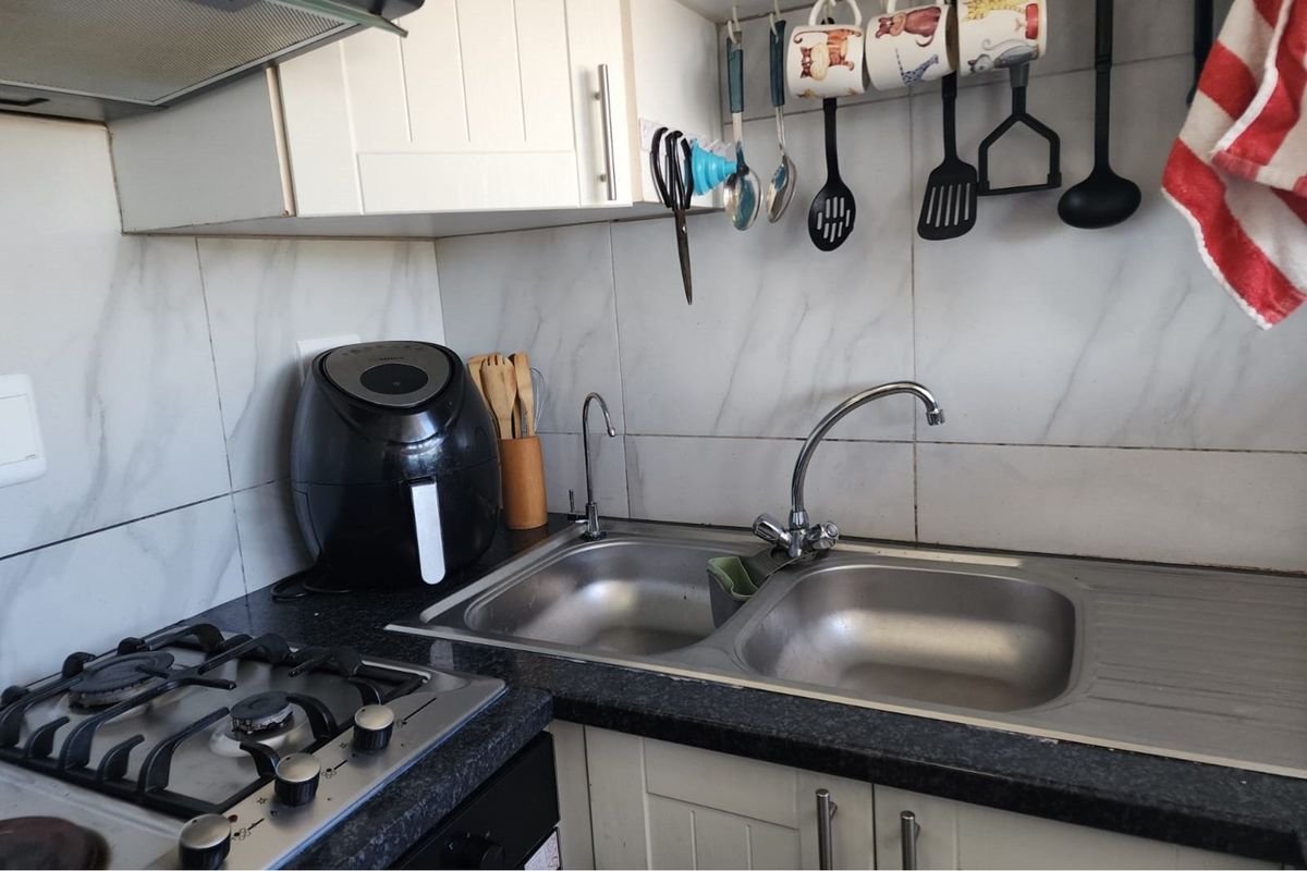 Compact kitchen area featuring a double stainless steel sink, gas hob, and white cabinetry with marble-effect wall tiling.