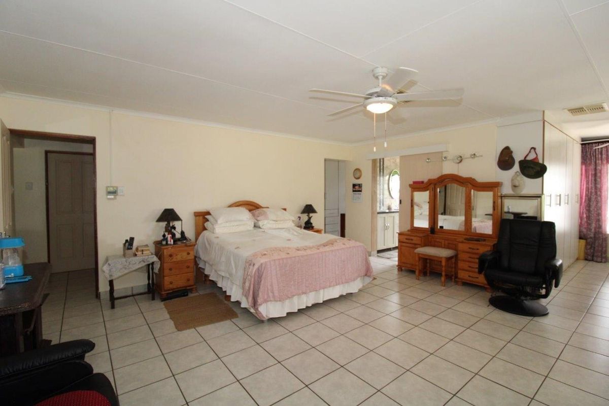 Spacious bedroom featuring tiled flooring, a ceiling fan, and built-in cupboards, with an adjoining en-suite bathroom area.