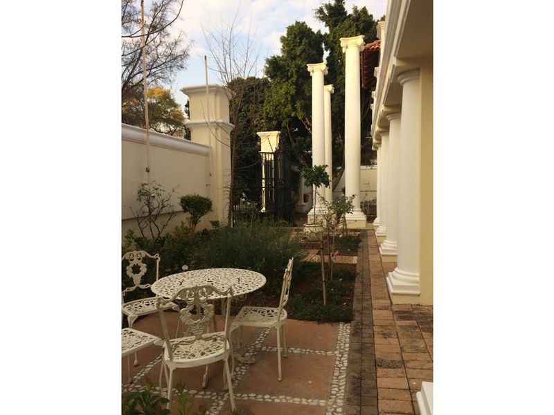 A classic patio area featuring decorative columns, paved flooring, and a landscaped garden border, providing an elegant outdoor space for relaxation.