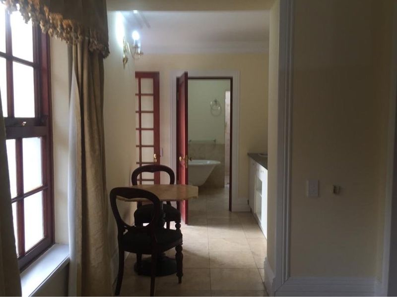A view through a hallway leading to a bathroom, featuring tiled flooring, traditional timber-framed windows, and classic interior door frames.