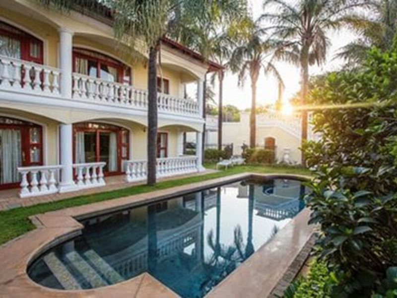 A view of the rear exterior featuring a swimming pool, landscaped garden, and a two-story building with balconies and classic architectural columns.