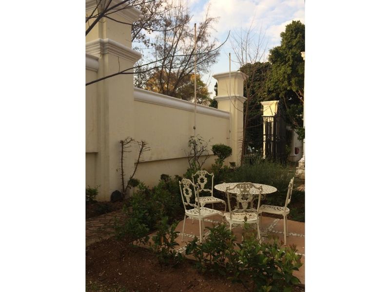 A private garden area featuring a paved patio space enclosed by a high boundary wall and mature landscaping.