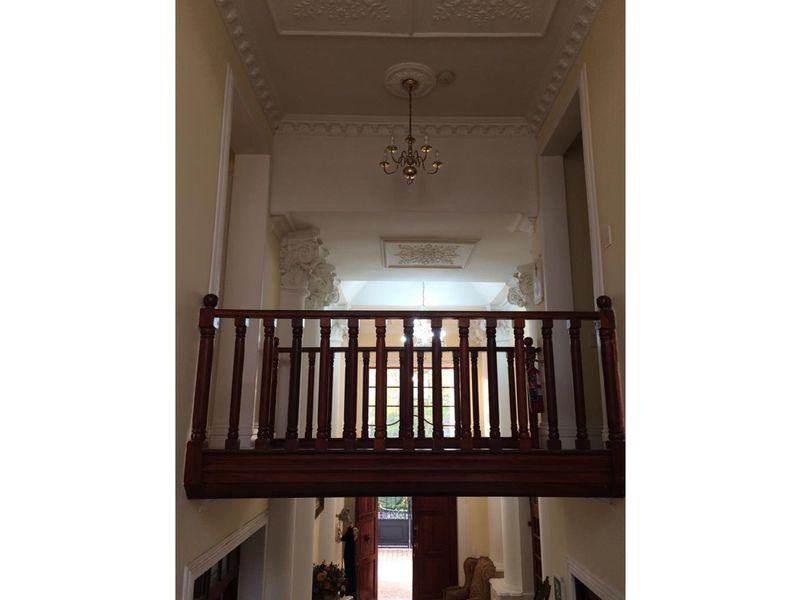 A grand interior hallway featuring a wooden balustrade, ornate ceiling cornicing, and decorative architectural columns, creating a classic and elegant entrance space.