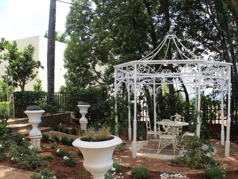 A landscaped garden area featuring a decorative wrought iron gazebo, brick paving, and established trees, providing a tranquil outdoor space.