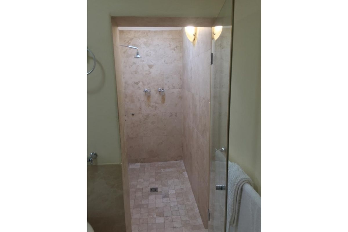A walk-in shower featuring natural stone wall and floor tiling, a glass door, and wall-mounted shower fixtures.