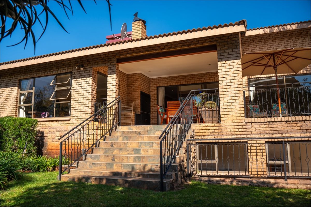 A rear exterior view of a brick house featuring a covered patio, stone-tiled staircase with wrought iron railings, and large windows.