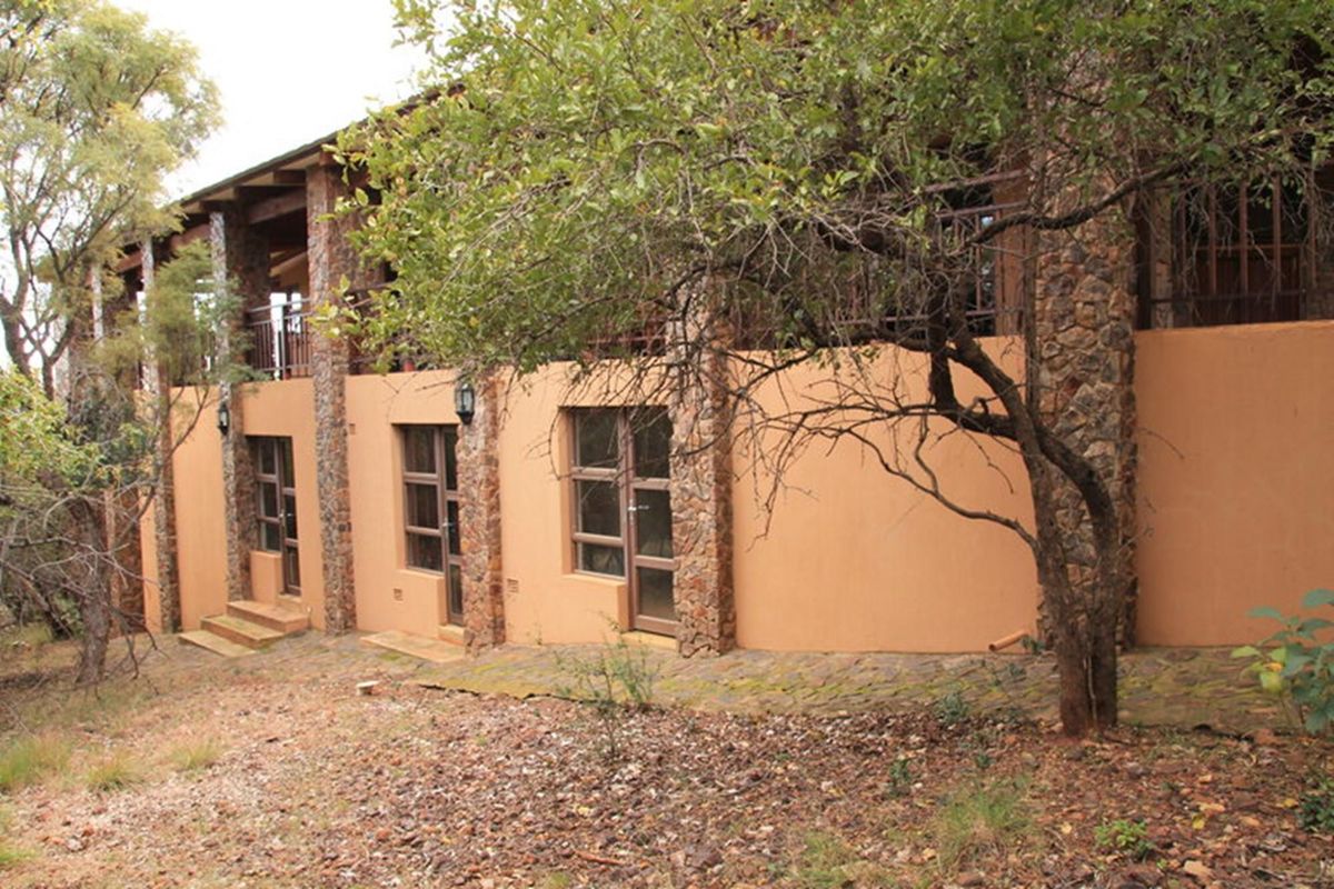 Rear exterior view of the property featuring stone-clad pillars, plastered walls, and a covered patio area overlooking the natural garden.