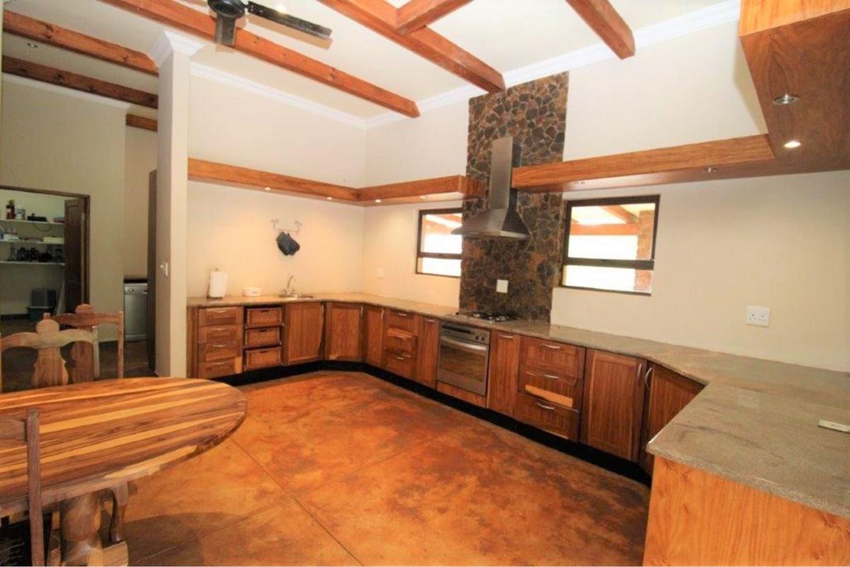Spacious kitchen featuring wooden cabinetry, stone-tiled backsplash, built-in oven and extractor fan, exposed timber ceiling beams, and polished concrete flooring.