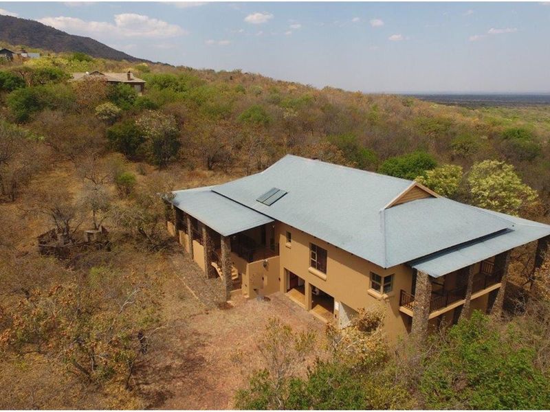 Aerial view of a multi-level residential property featuring a pitched metal roof, stone-clad pillars, and expansive wrap-around balconies set in a natural bushveld landscape.