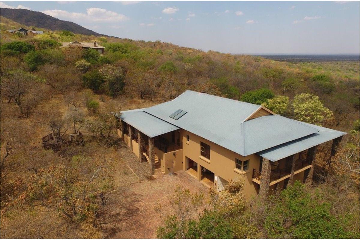 Aerial view of a multi-level residential property featuring a pitched metal roof, stone-clad pillars, and expansive wrap-around balconies set in a natural bushveld landscape.