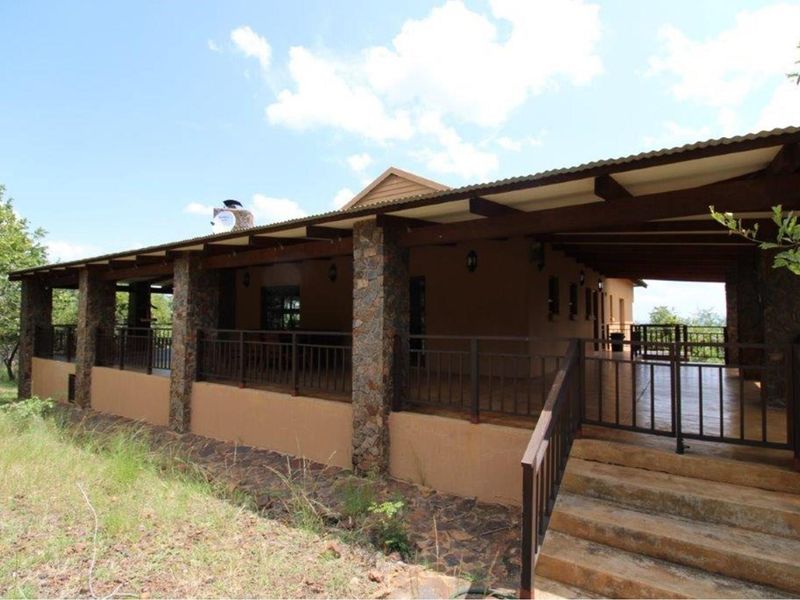 A spacious covered patio featuring stone-clad pillars, metal railings, and concrete stairs, offering an expansive outdoor living area.