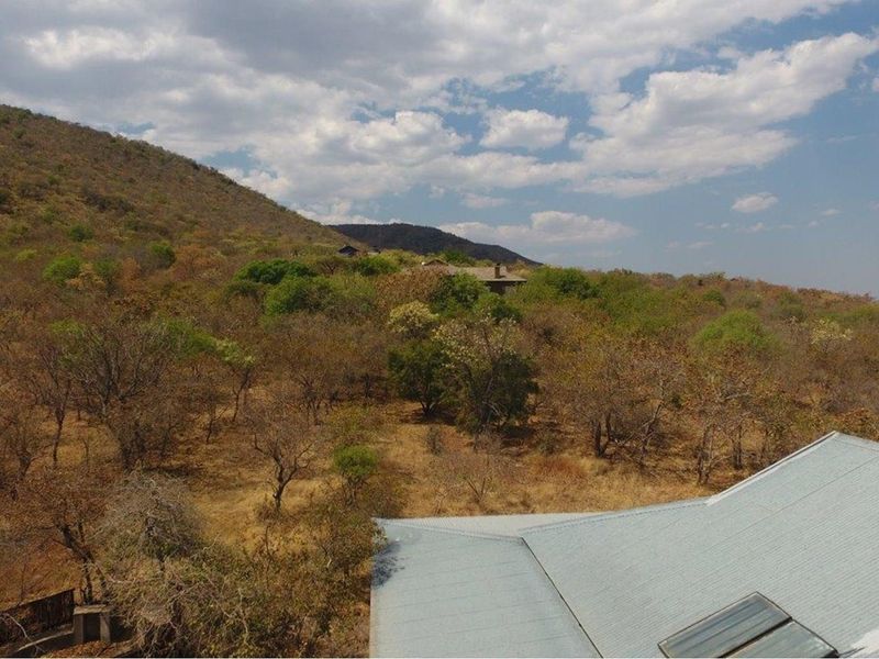 An elevated aerial view showcasing the property's metal roof, solar water heating system, and the surrounding natural bushveld landscape.
