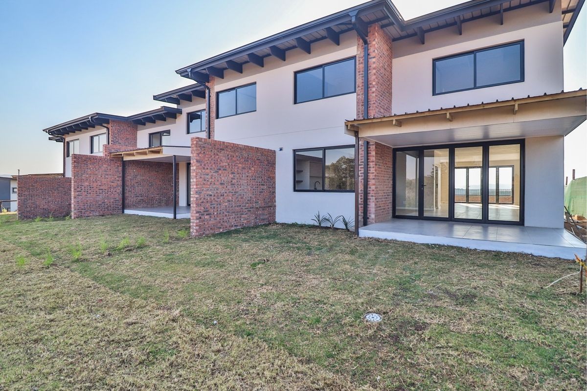 Rear view of a modern townhouse complex featuring exposed brick accents, covered patios, and large sliding glass doors opening onto a private garden area.