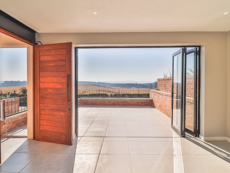 Bright living area featuring large bi-fold doors opening onto a spacious tiled patio with scenic landscape views.