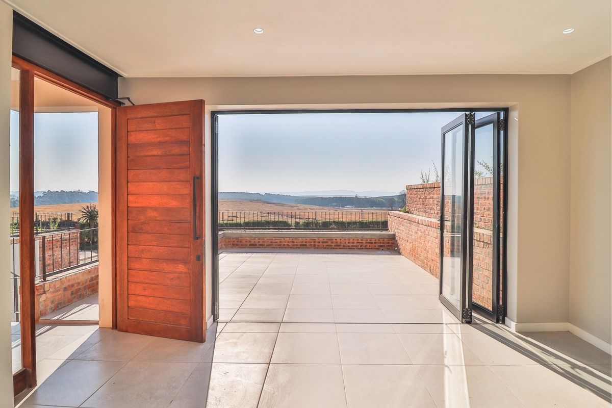 Bright living area featuring large bi-fold doors opening onto a spacious tiled patio with scenic landscape views.