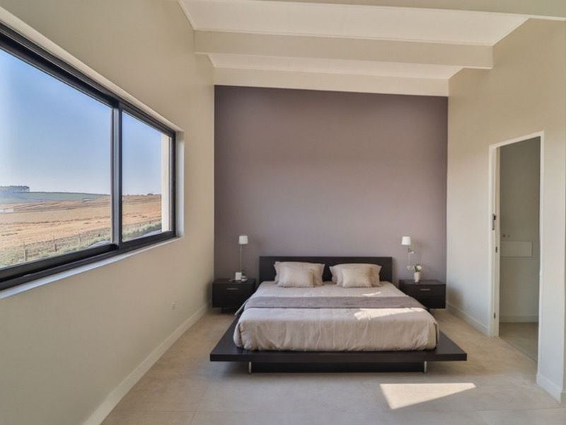 Spacious bedroom featuring high ceilings, a large window with scenic landscape views, and a neutral color palette with a feature wall.