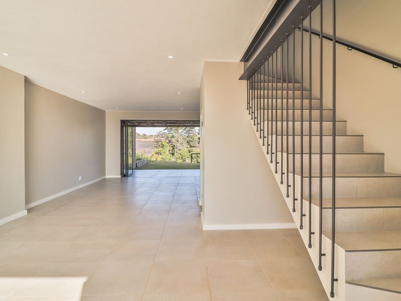 Spacious open-plan living area featuring modern tiled flooring, recessed ceiling lighting, and a contemporary staircase with a sleek metal balustrade leading to the upper level.