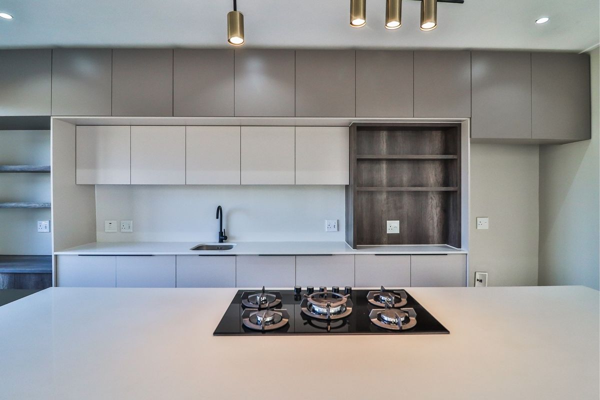 Modern kitchen featuring sleek handleless cabinetry, a central island with a built-in gas hob, stone countertops, and integrated shelving.
