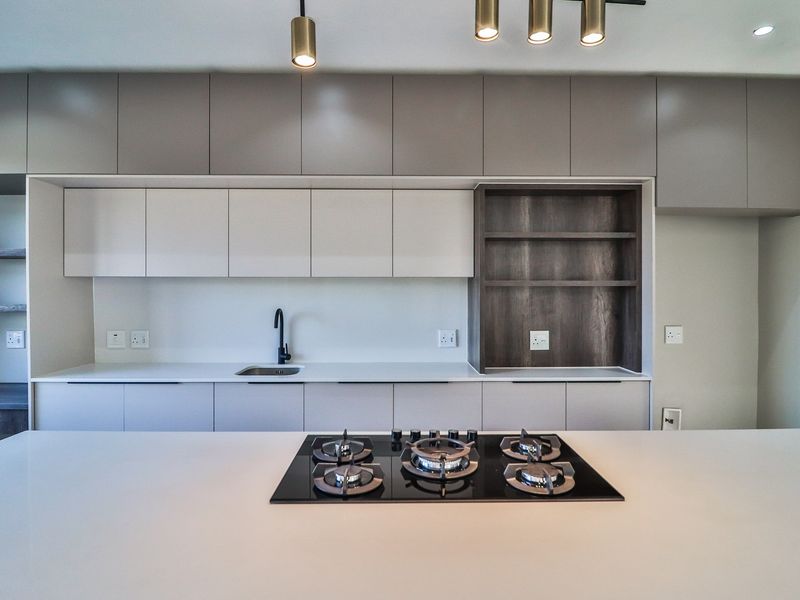 Modern kitchen featuring sleek handleless cabinetry, a central island with a built-in gas hob, stone countertops, and integrated shelving.