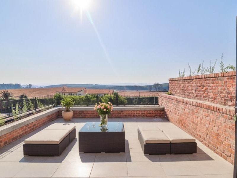 A spacious rooftop terrace featuring exposed brick retaining walls, tiled flooring, and panoramic views of the surrounding landscape.