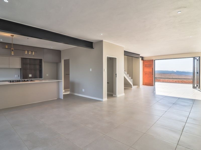 Spacious open-plan living area featuring a modern kitchen with stone countertops, integrated gas hob, and seamless flow to a large outdoor balcony.