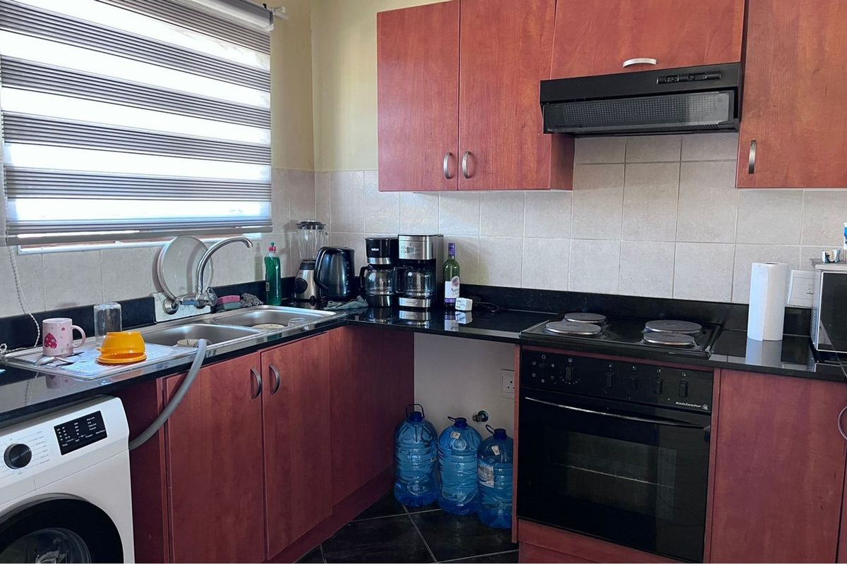 A functional kitchen featuring dark granite countertops, cherry-wood tone cabinetry, a built-in oven with hob, and an integrated extractor fan.
