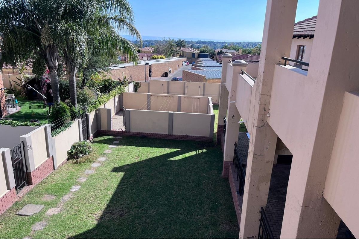Elevated view of a private garden area featuring a lawn, paved pathway, and perimeter walling, viewed from an upper-level balcony.