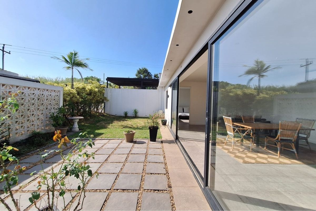 A private rear garden featuring a paved patio area, lawn, and large sliding glass doors providing seamless indoor-outdoor flow to the living space.
