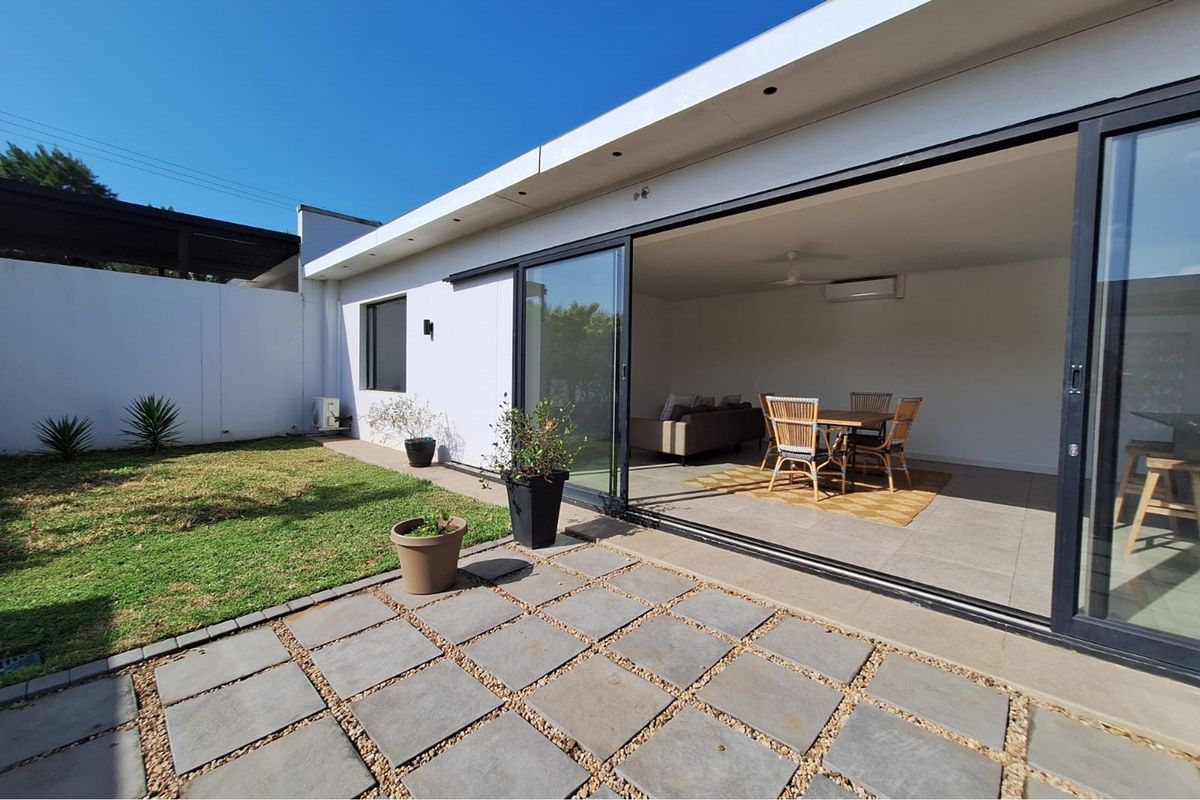 A modern townhouse featuring a seamless transition from the interior living space to a paved patio and private garden area through large sliding doors.