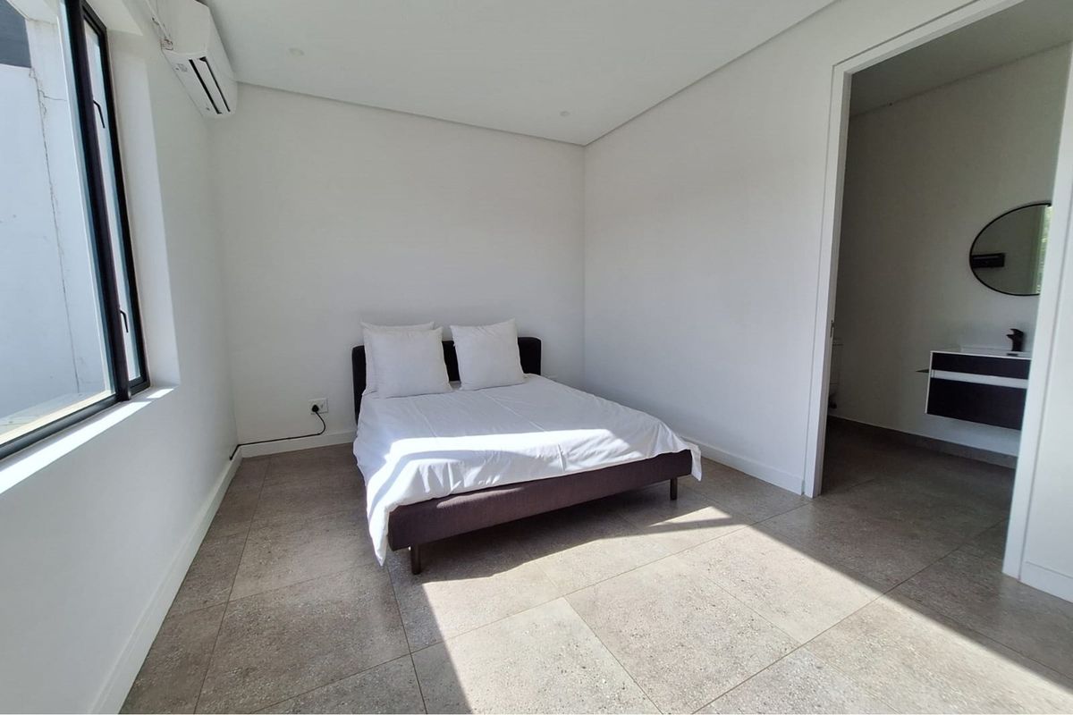 A bright bedroom featuring large format floor tiles, a wall-mounted air conditioning unit, and an en-suite bathroom.